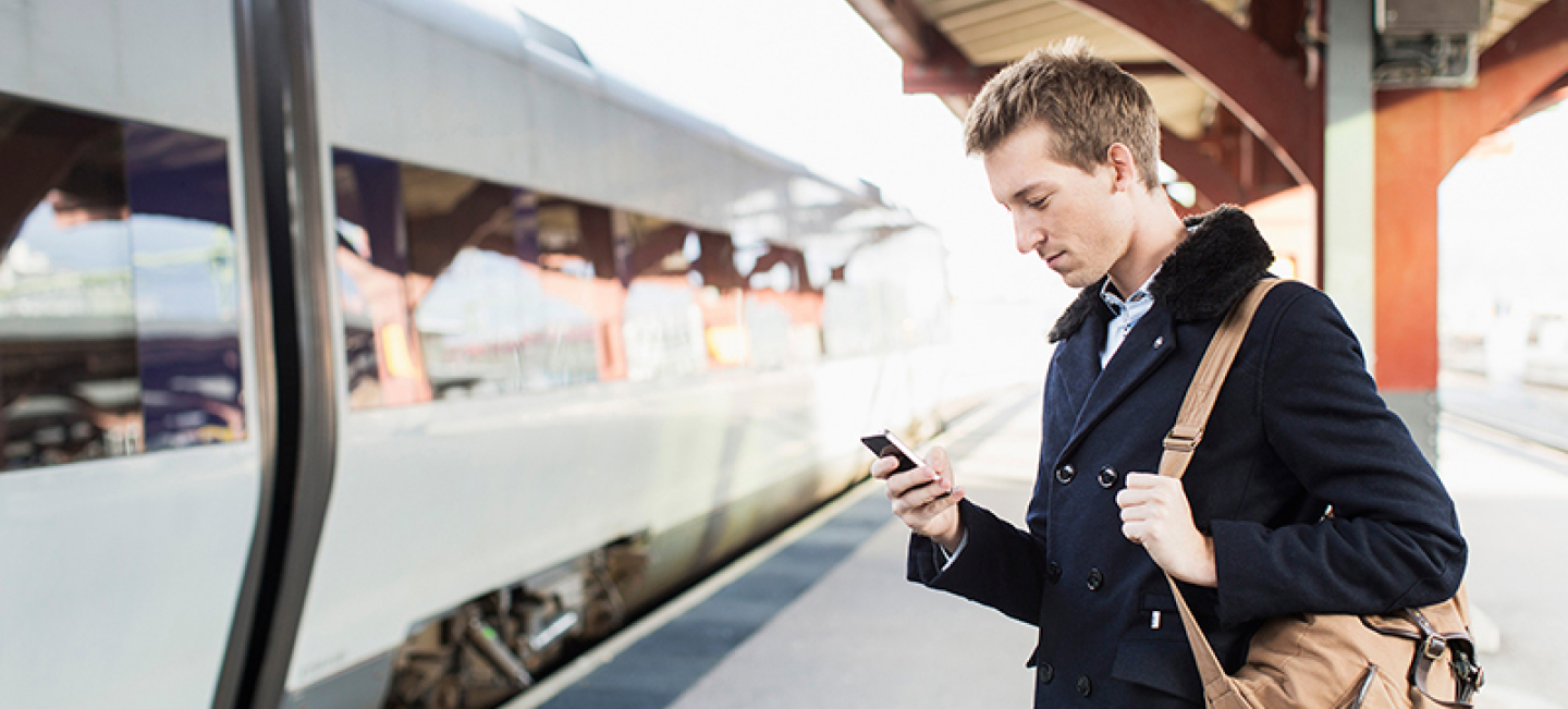 En man tittar på sin mobiltelefon för att kontrollera när tåget går.